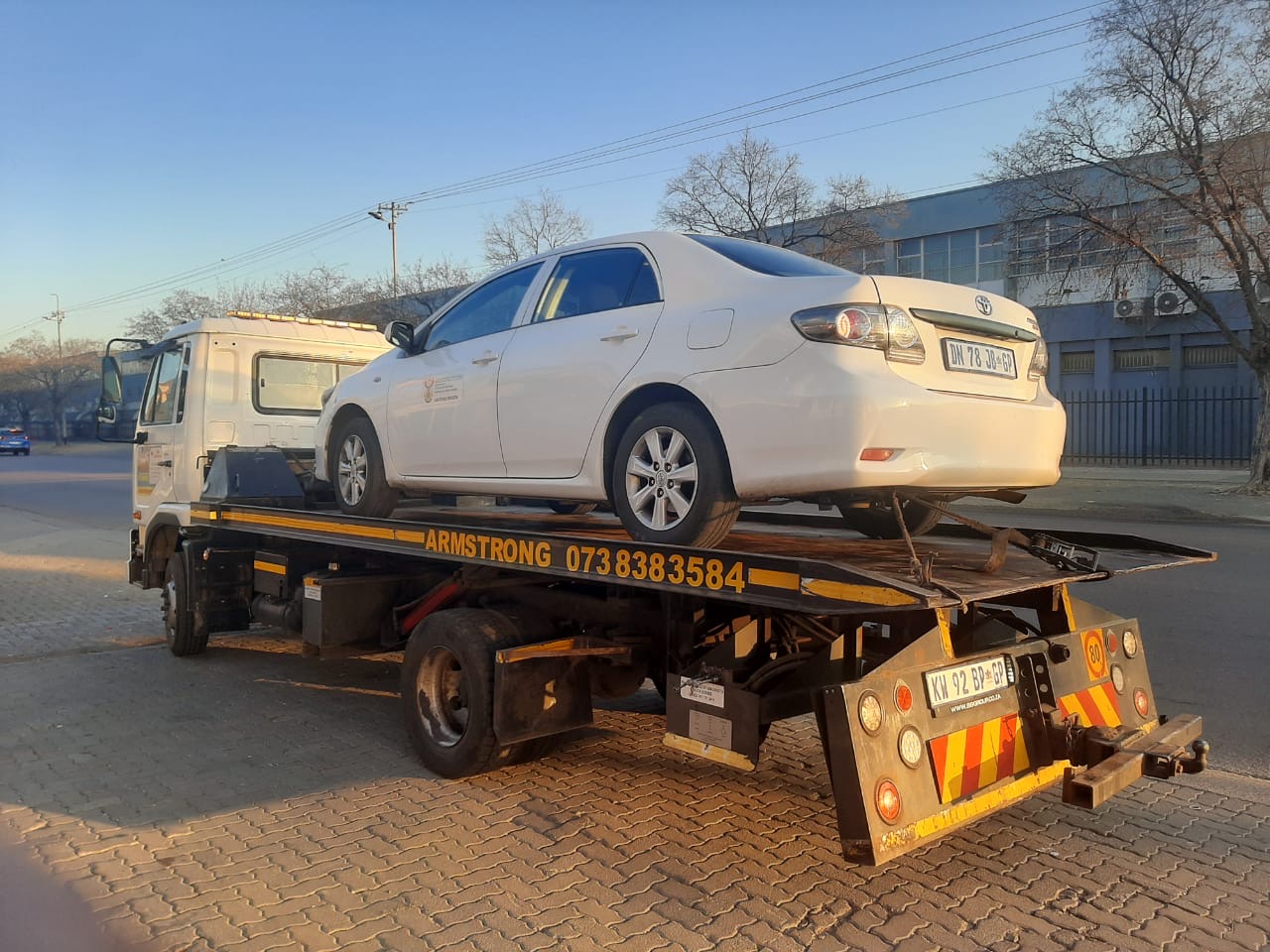 White Toyota Corolla loaded on the Armstrong Towing flatbed at sunrise