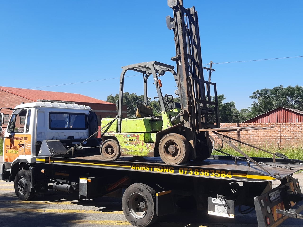 Armstrong Towing flatbed truck carrying a green forklift in daylight